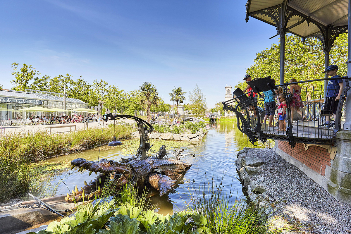 Family playing with the mechanical crocodile of the Place Napoléon Animals in La Roche-sur-Yon